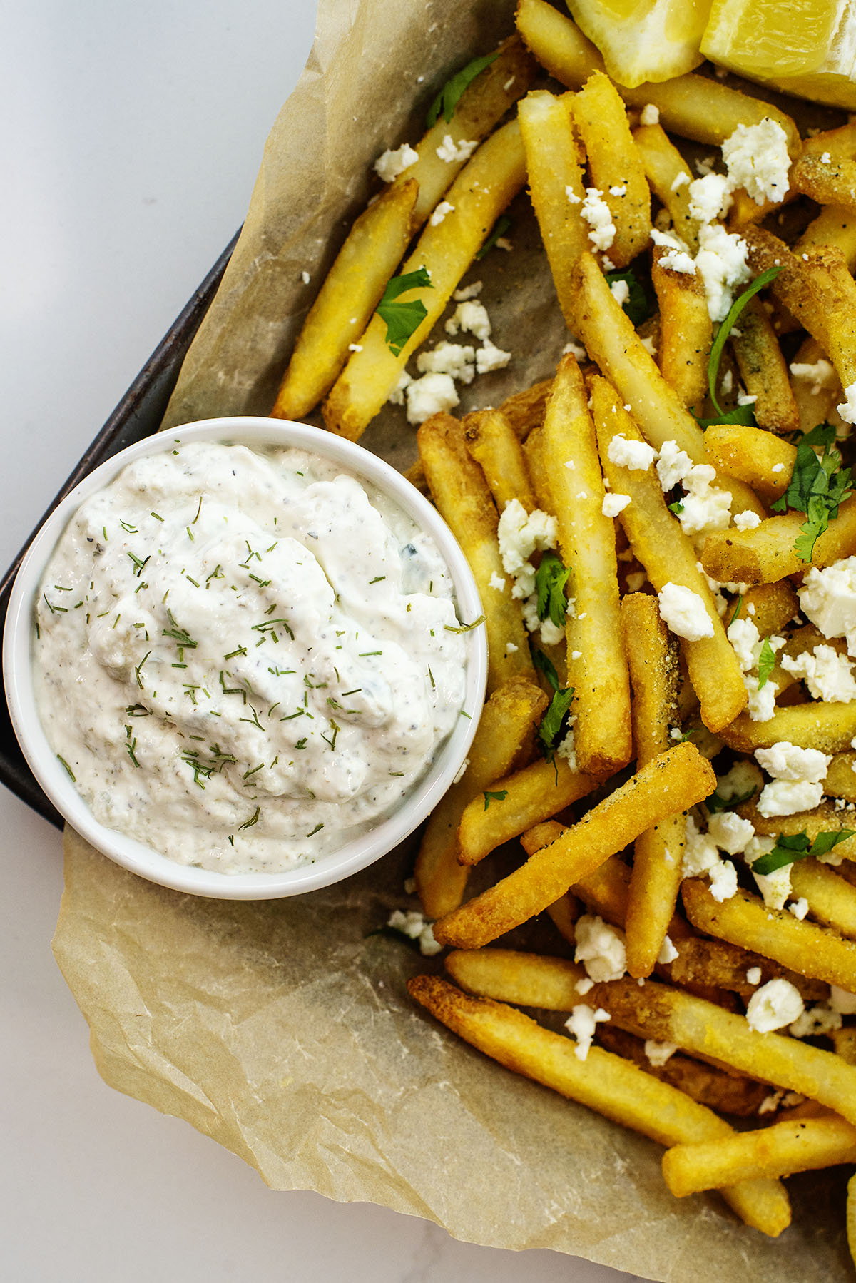 Close up of French fries with feta cheese and seasoning on them with a cup of tatziki sauce.