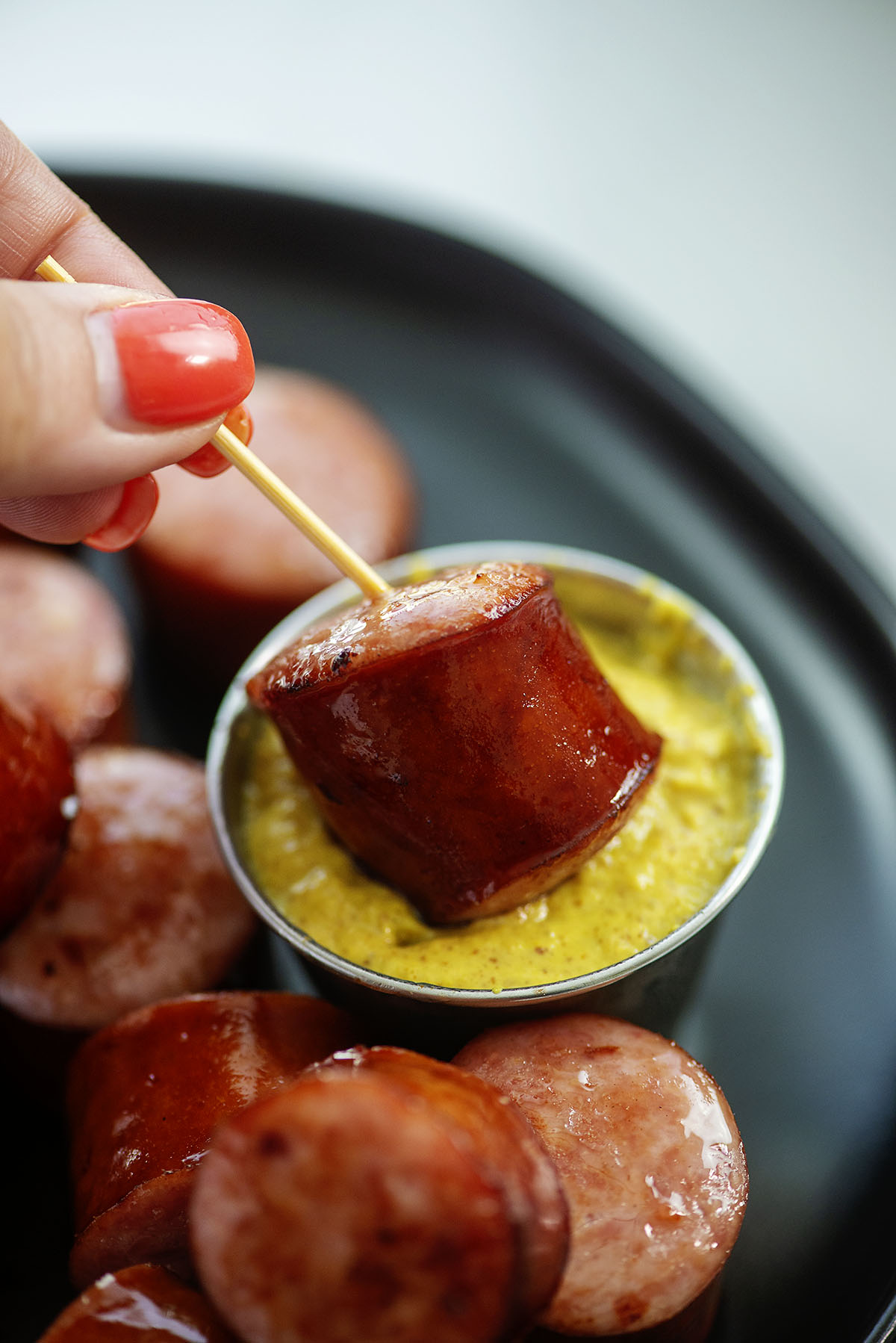 A woman dipping a smoked sausage in mustard.