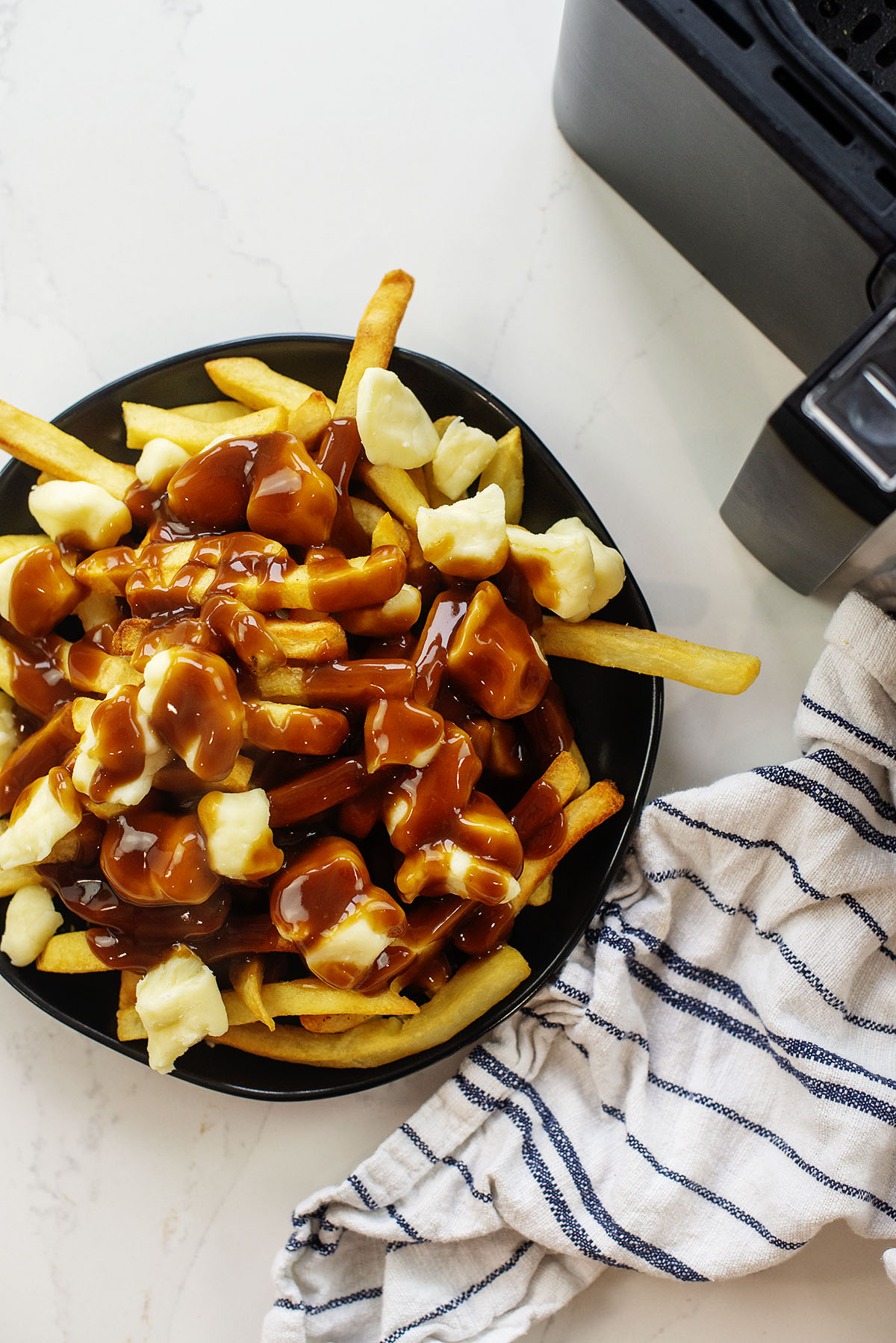 A plate of poutine in front of an air fryer basket.