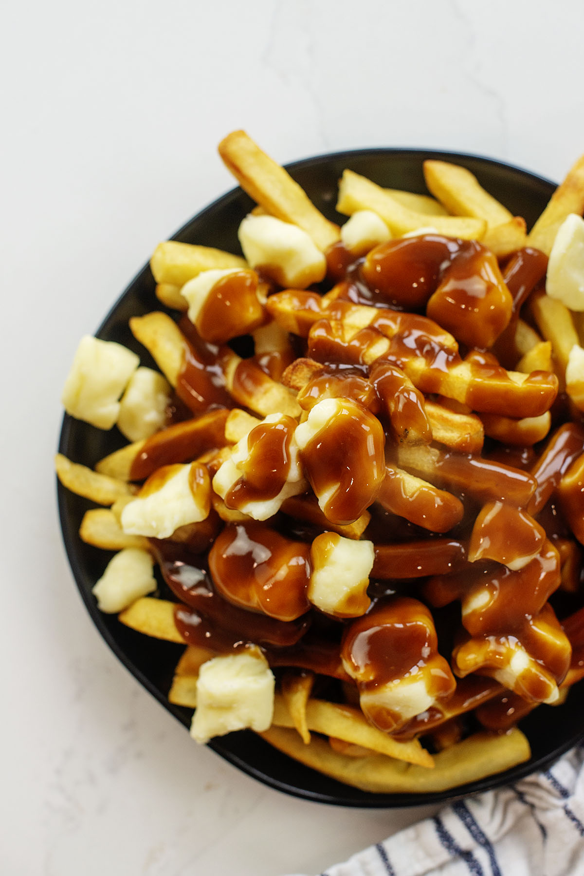 Overhead view of poutine on a small black plate.