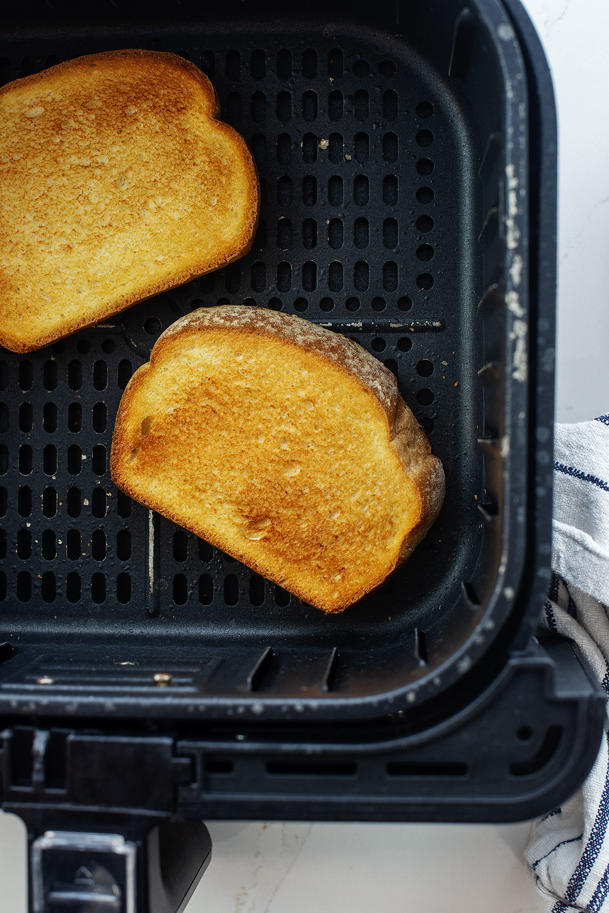 Two slices of toast in an air fryer basket.