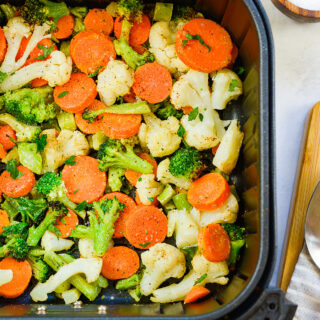 Seasoned veggies in an air fryer basket.