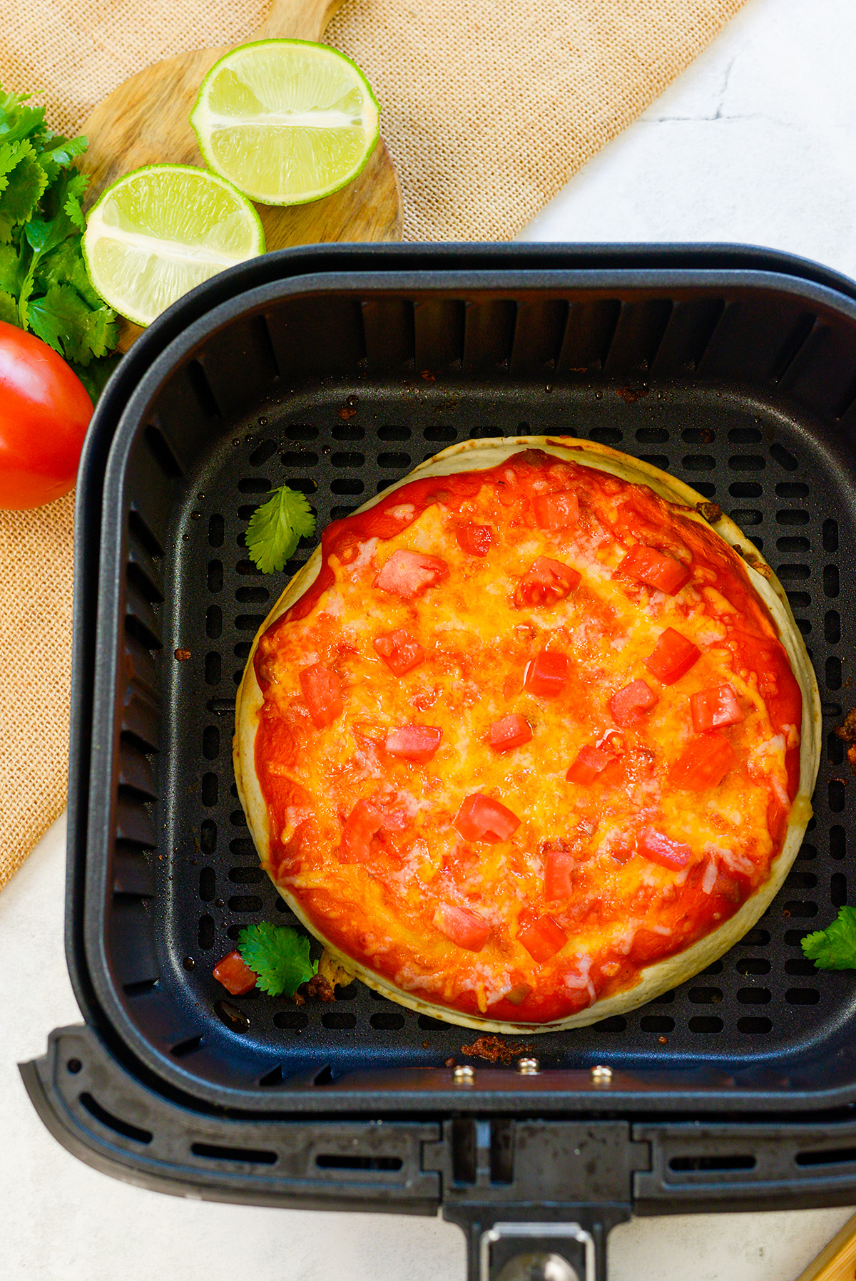 Overhead view of a Mexican pizza in an air fryer basket.