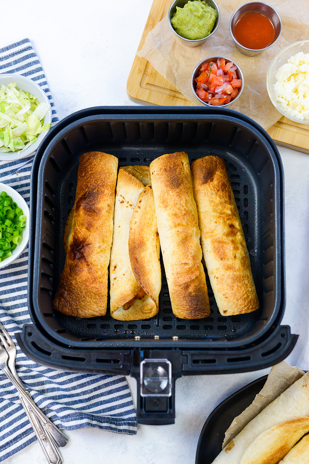 Four cooked flautas in an air fryer basket.