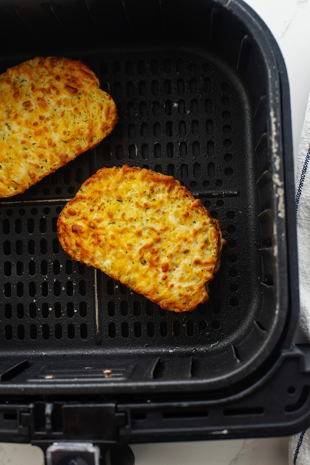Two slices of garlic cheese bread in an air fryer basket.