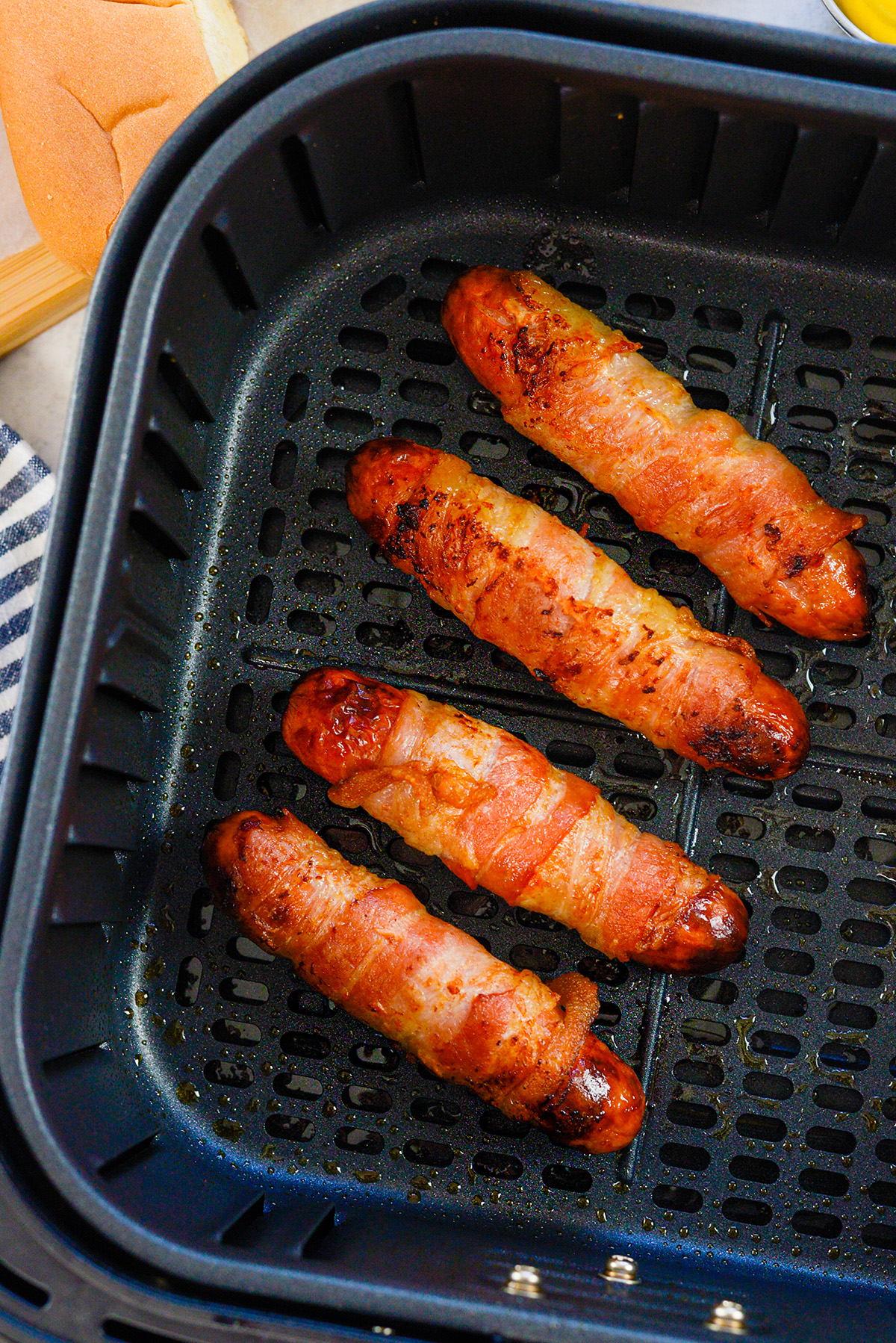 Four bacon wrapped hot dogs lined up in an air fryer basket.