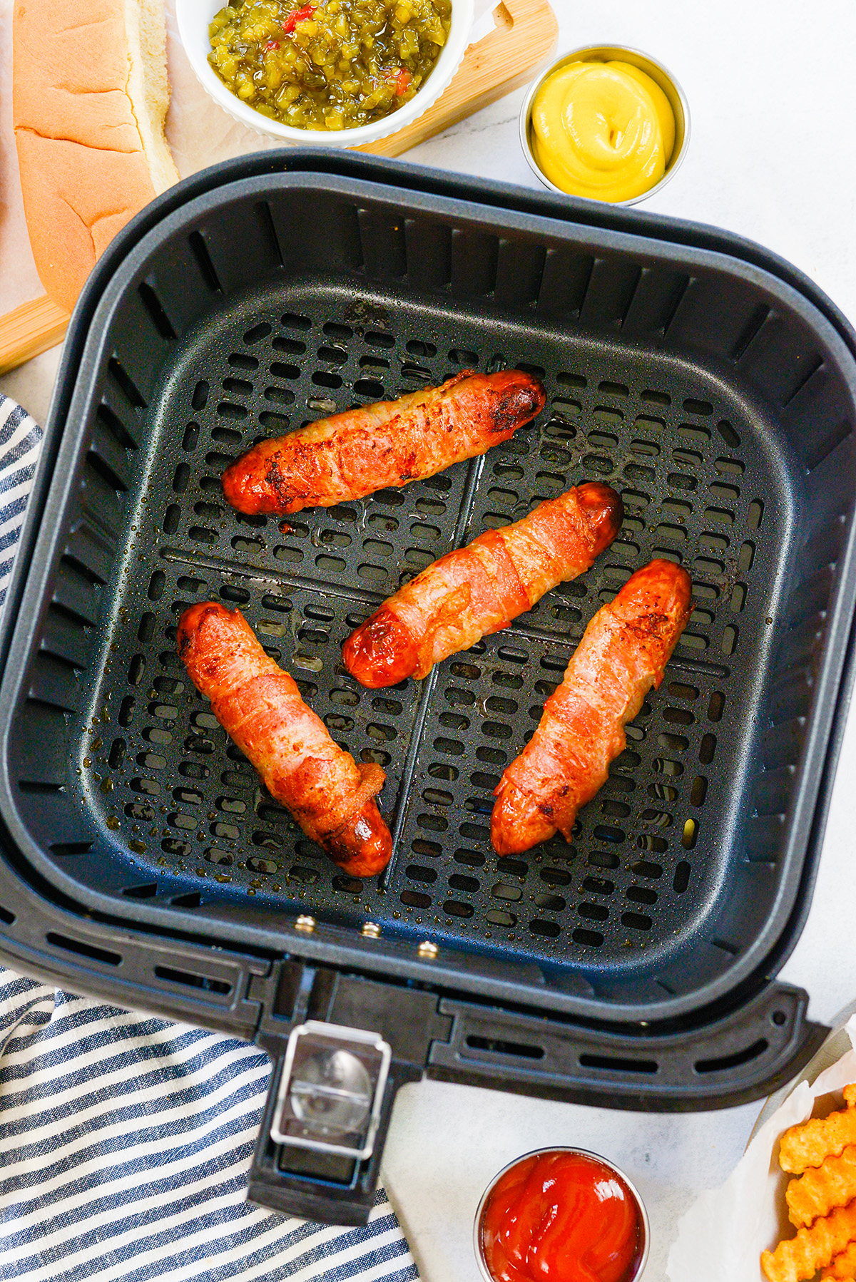 Four cooked bacon wrapped hot dogs in an air fryer basket.