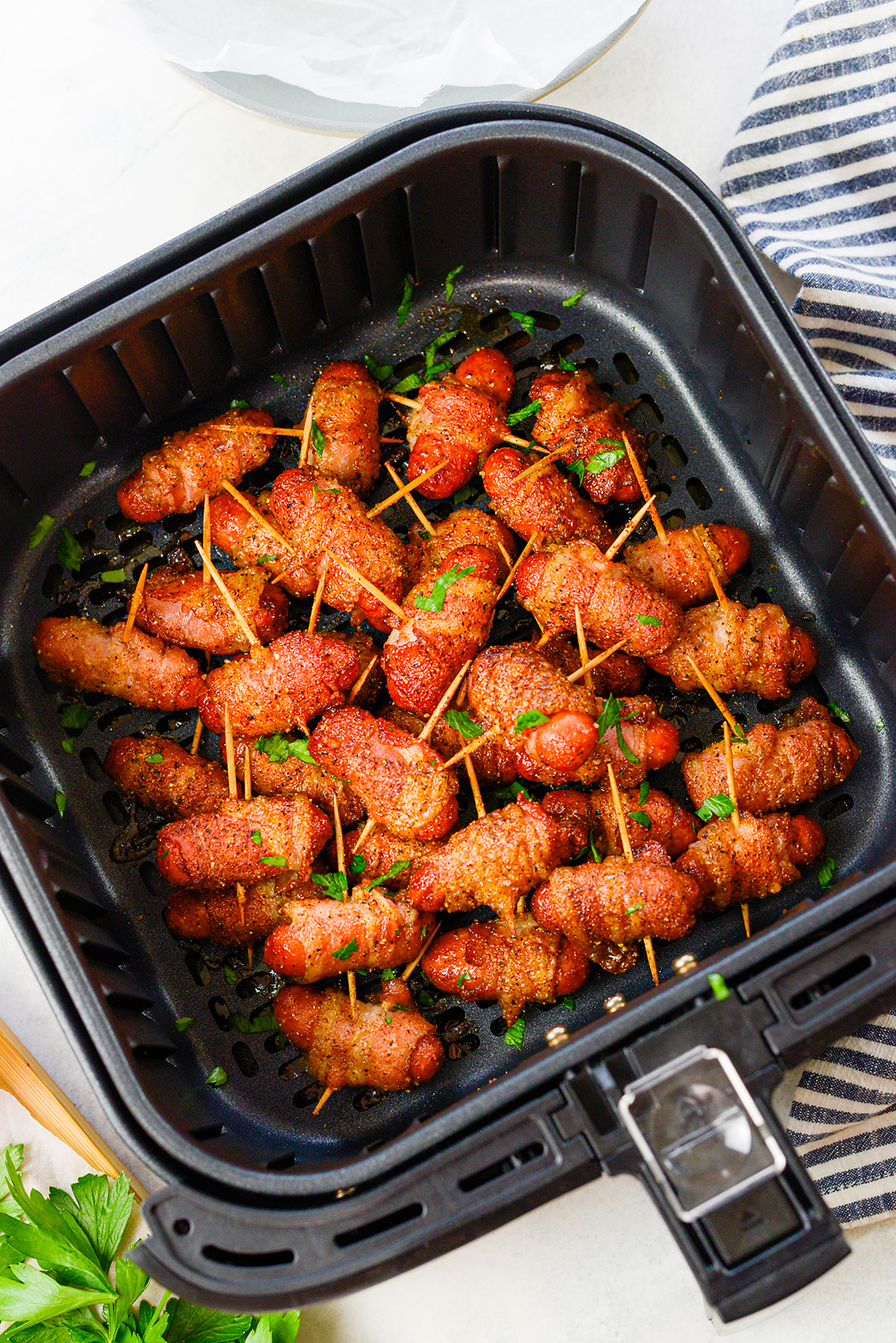 Overhead view of an air fryer basket full of bacon wrapped lil smokies.