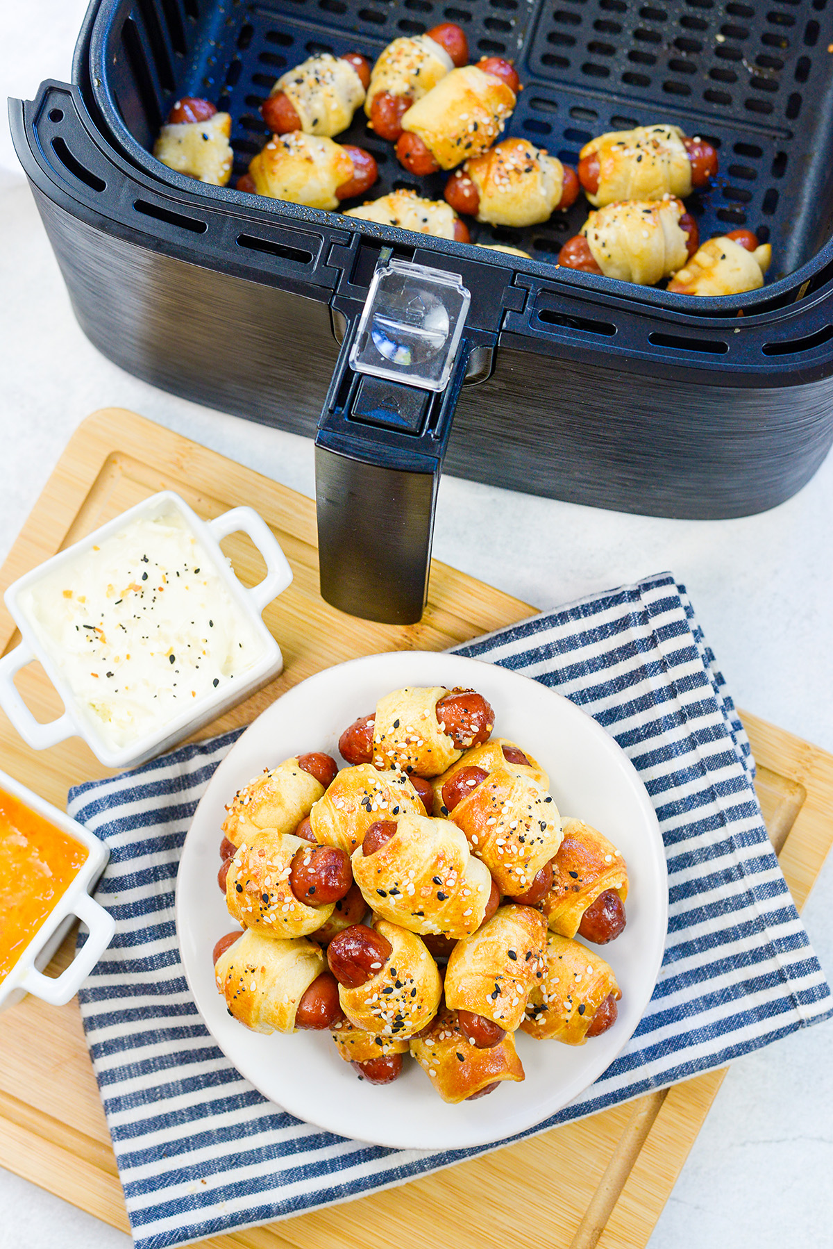 A plate full of mini pigs in a blanket in front of an air fryer.