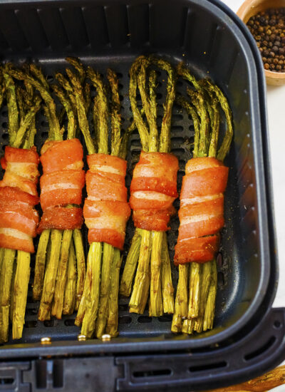 Close up of bacon wrapped asparagus in an air fryer basket.