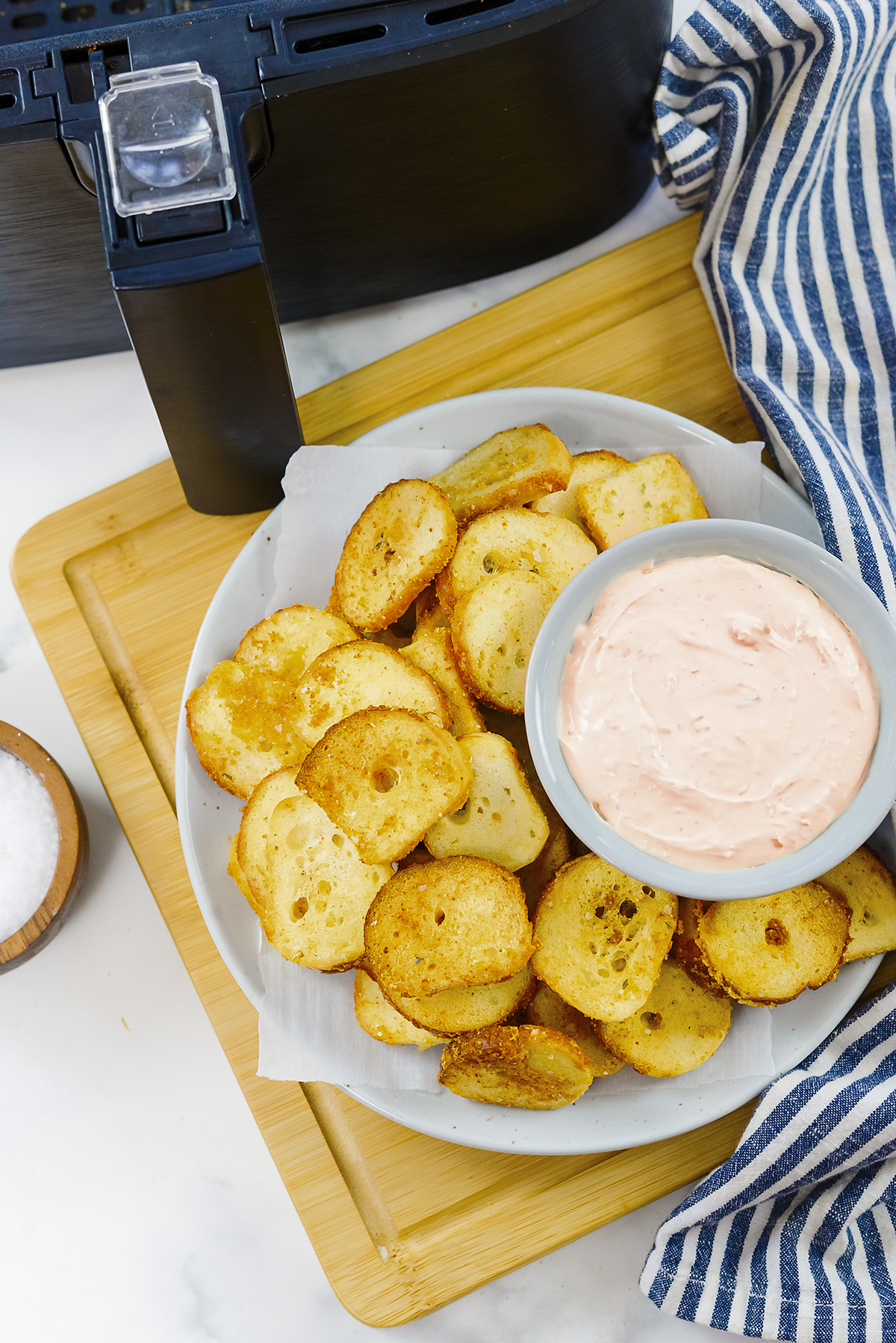 Overhead view of cooked bagel chips in front of an air fryer basket.