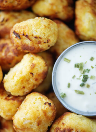 Close up of cauliflower tots stacked up next to a cup of ranch dressing.