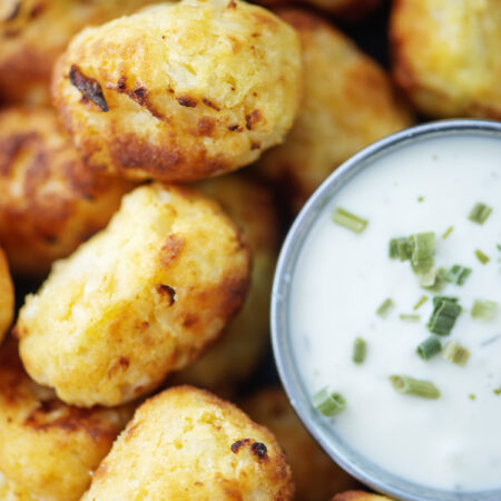 Close up of cauliflower tots stacked up next to a cup of ranch dressing.