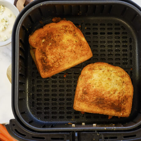 Two buffalo chicken grilled cheese sandwiches in an air fryer basket.