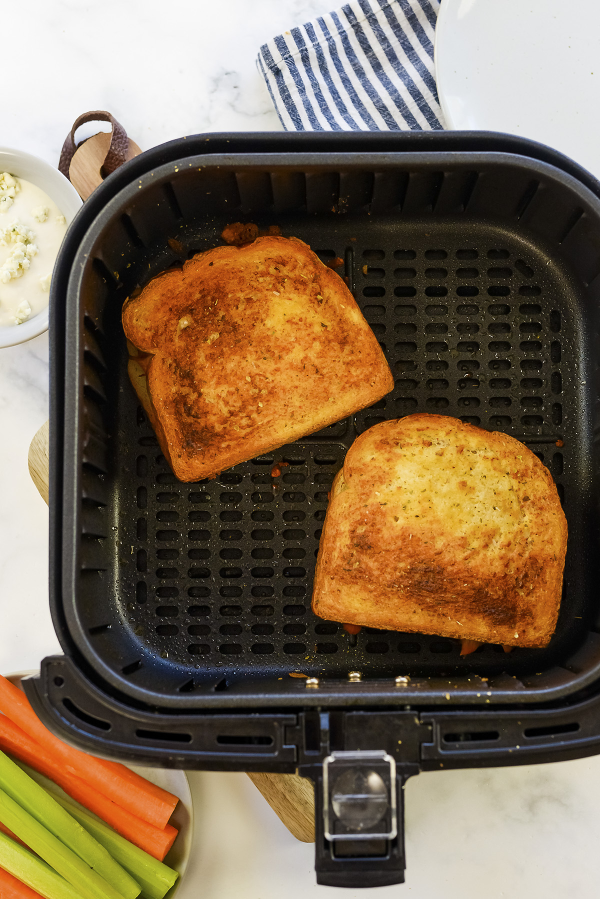 Two buffalo chicken grilled cheese sandwiches in an air fryer basket.
