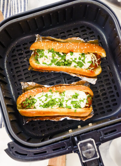 Two meatball subs resting on foil inside an air fryer basket.