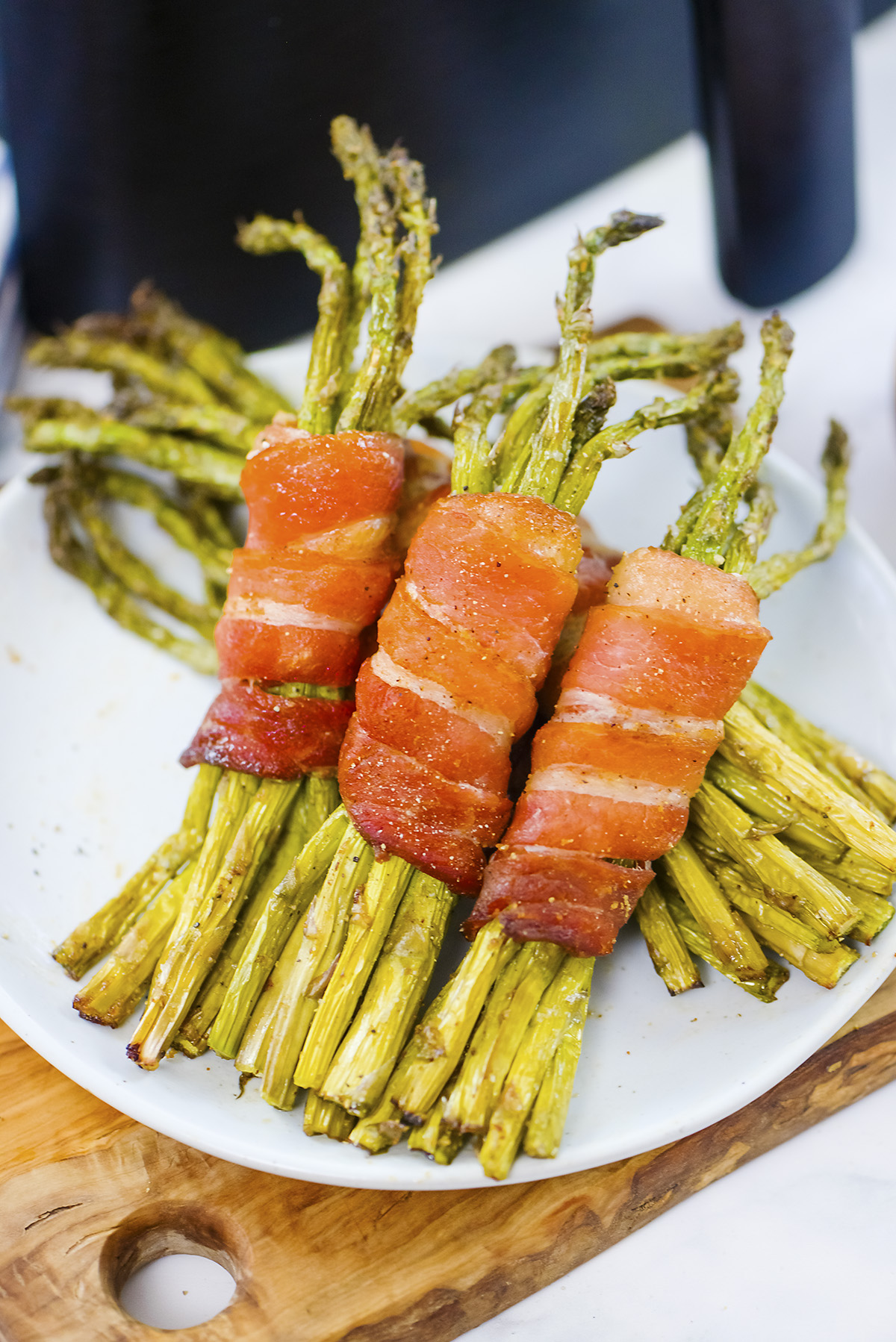 Bacon wrapped asparagus stacked on a white plate.