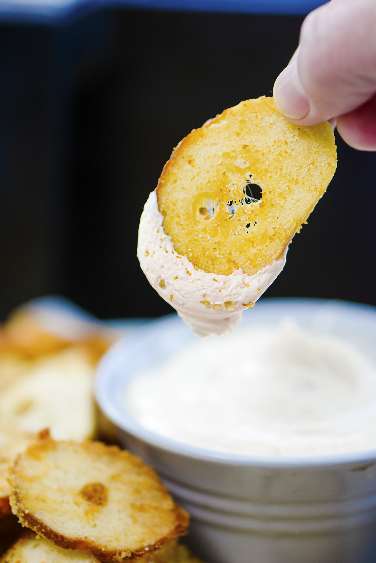 A bagel chip being dipped into cream cheese.