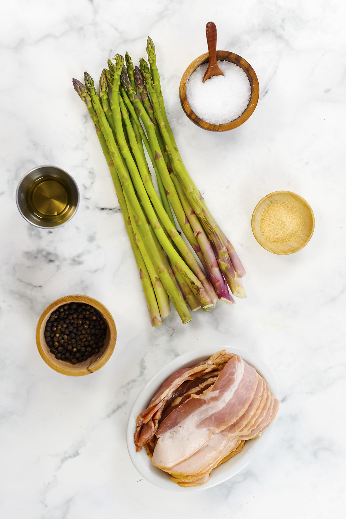Ingredients for bacon wrapped asparagus on a white countertop.