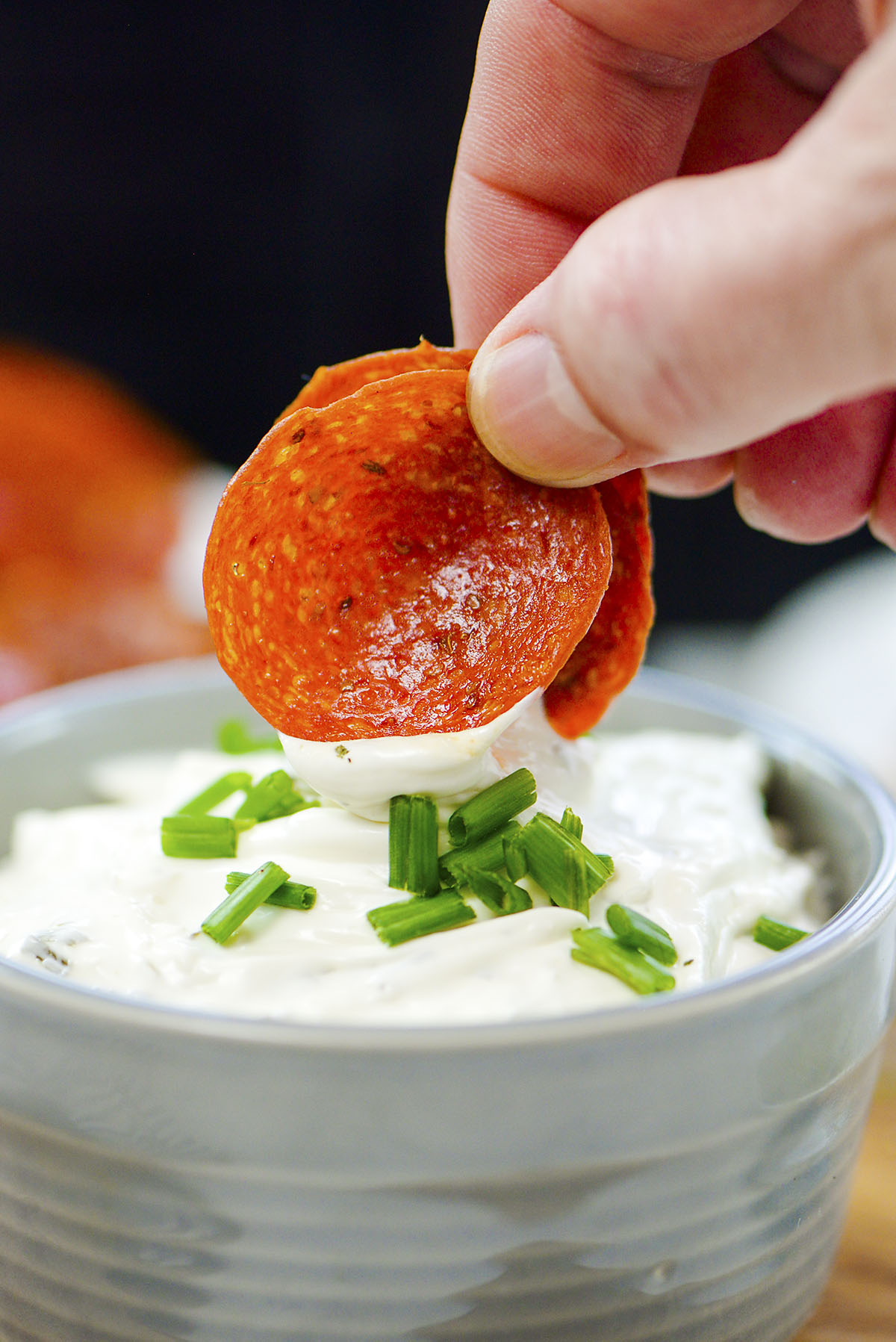 Close up of a pepperoni chip being dipped into ranch dressing.