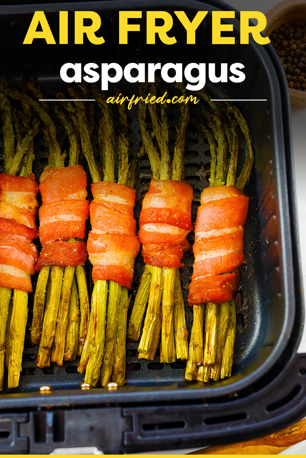 Bacon wrapped asparagus lined up in an air fryer basket.