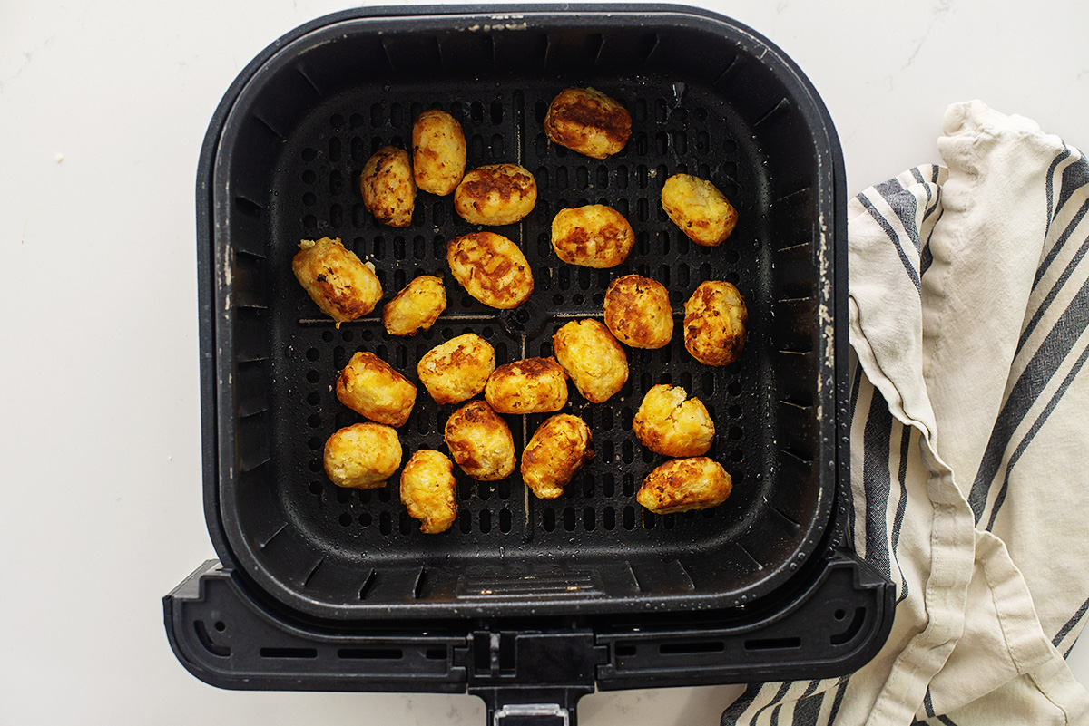 Cooked cauliflower tots in an air fryer basket.