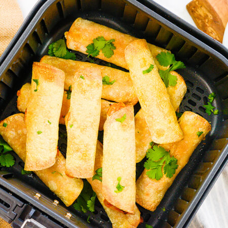 Chicken taquitos stacked up in an air fryer basket.