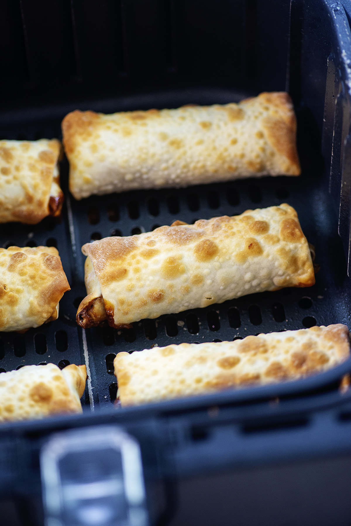 Six cooked snickers egg rolls in an air fryer basket.