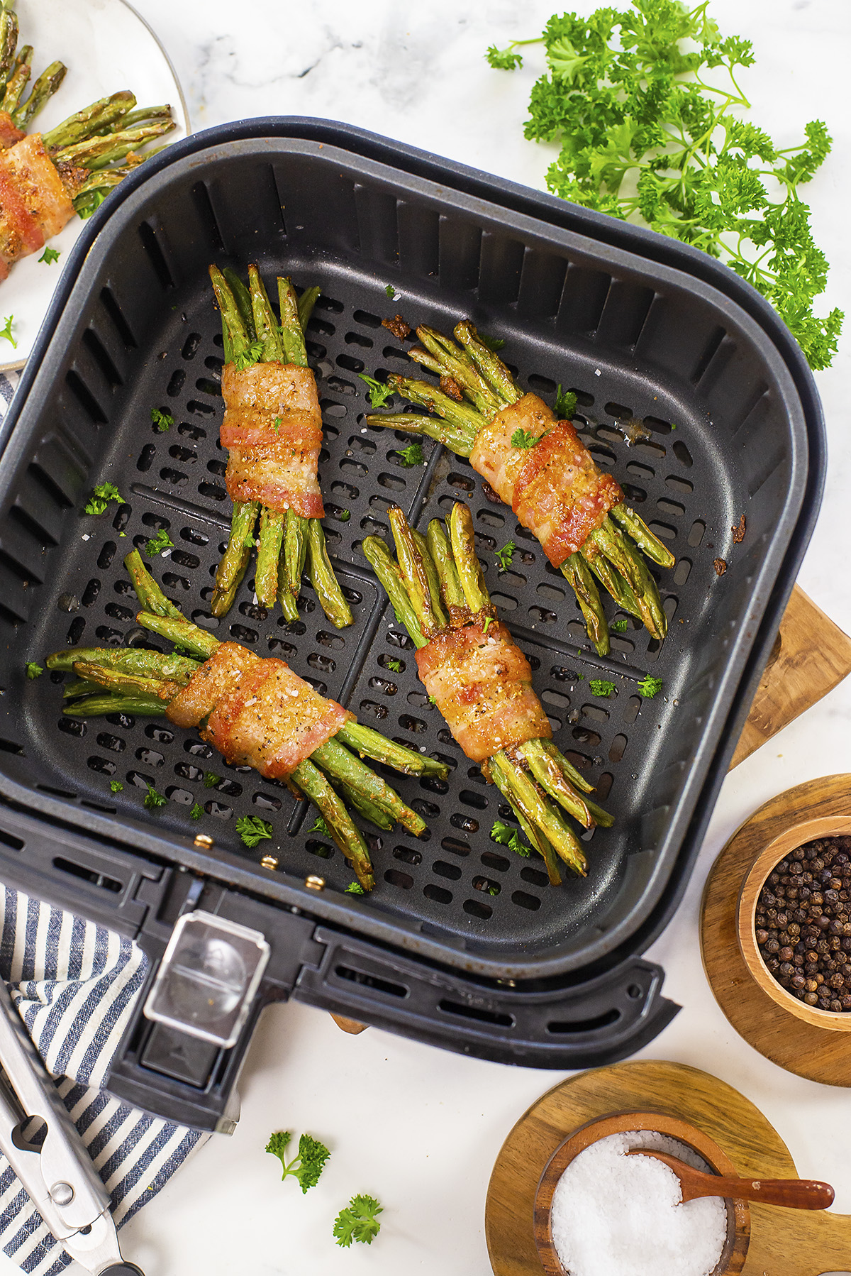 Four bundles of cooked bacon wrapped green beans in an air fryer basket.