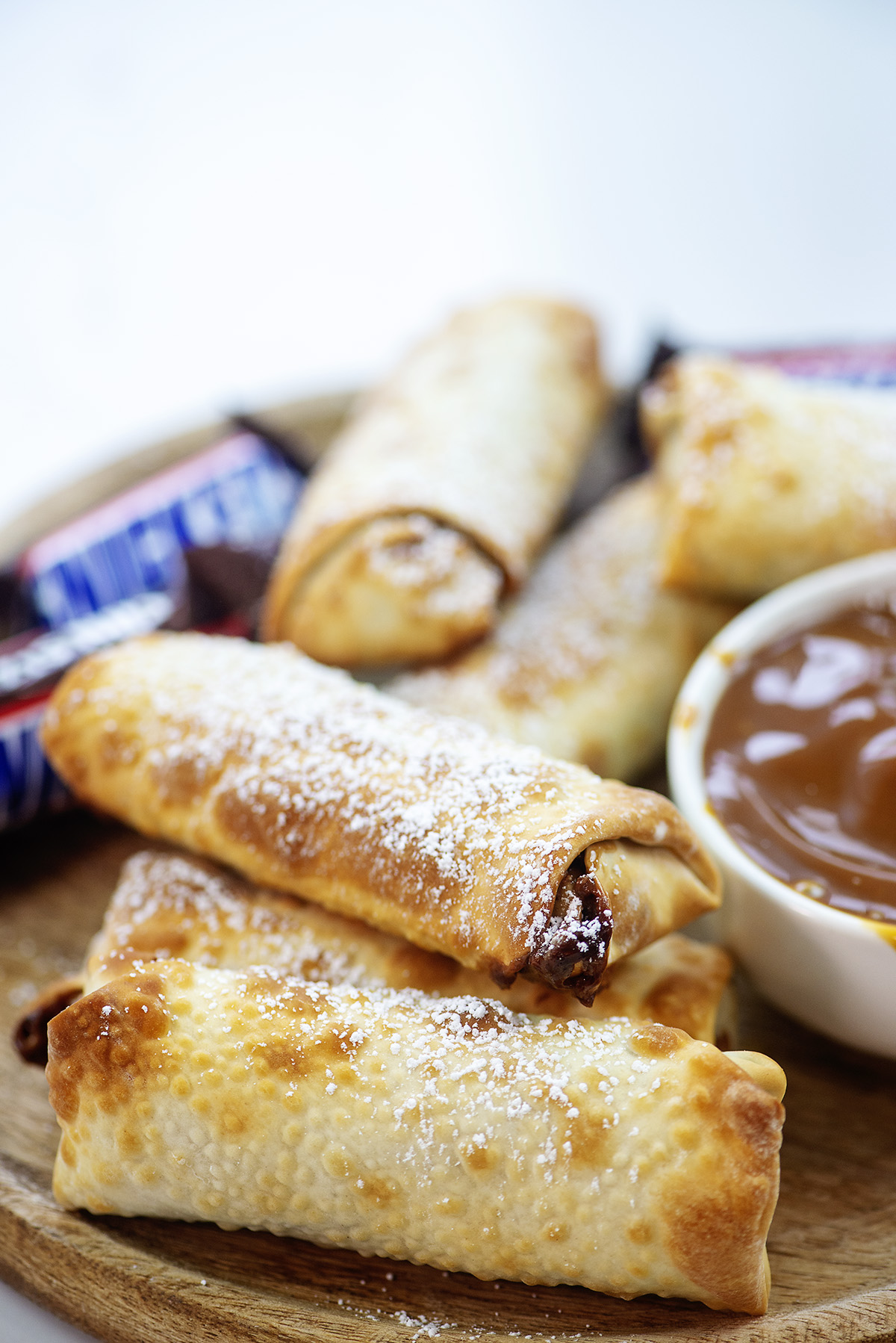 A few snickers egg rolls stacked on a wood tray.