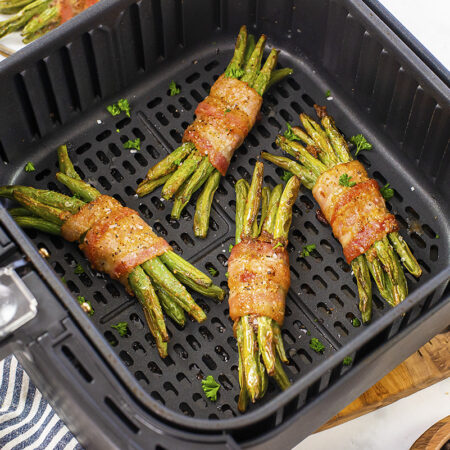 Four bundles of bacon wrapped green beans in an air fryer basket.