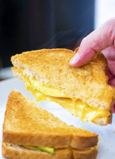 A person picking up half an avocado grilled cheese sandwich.
