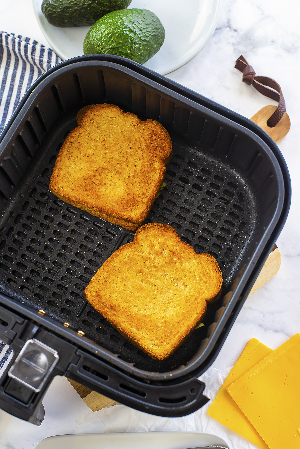 Two avocado grilled cheese sandwiches in an air fryer basket.