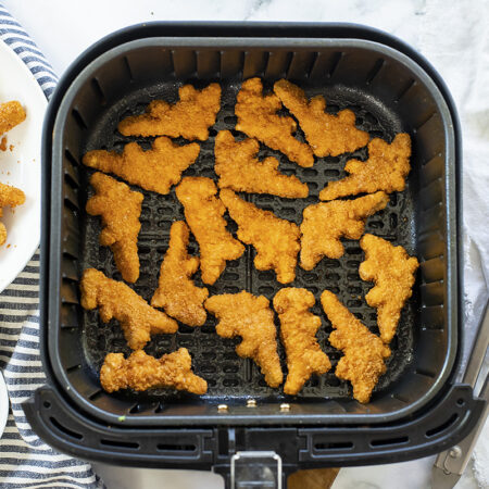 A plate of dino nuggets next to an air fryer basket.
