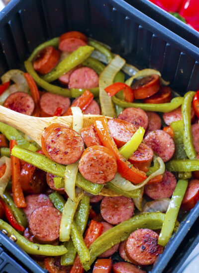 Sausage, peppers, and onions on a wooden spoon.