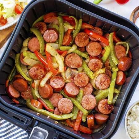Sausage, peppers, and onions in an air fryer basket.