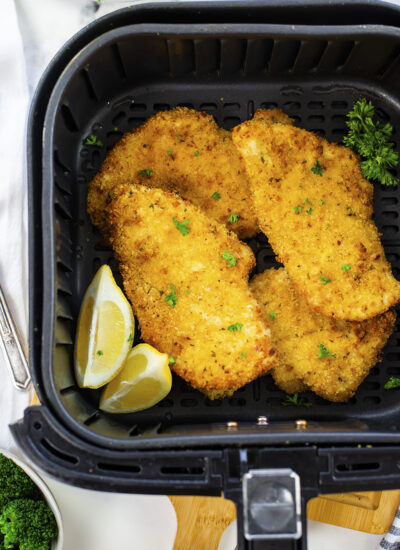 Four cooked chicken cutlets in an air fryer basket.