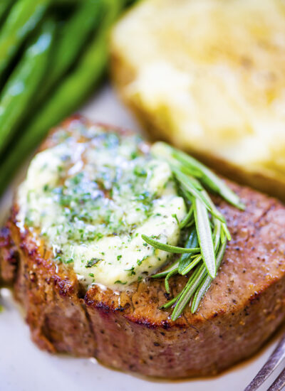 Close up of filet mignon topped with butter and herbs.