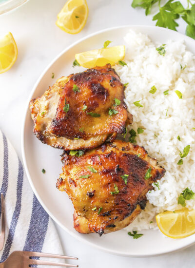 Lemons, rice, and chicken thighs on a white plate.
