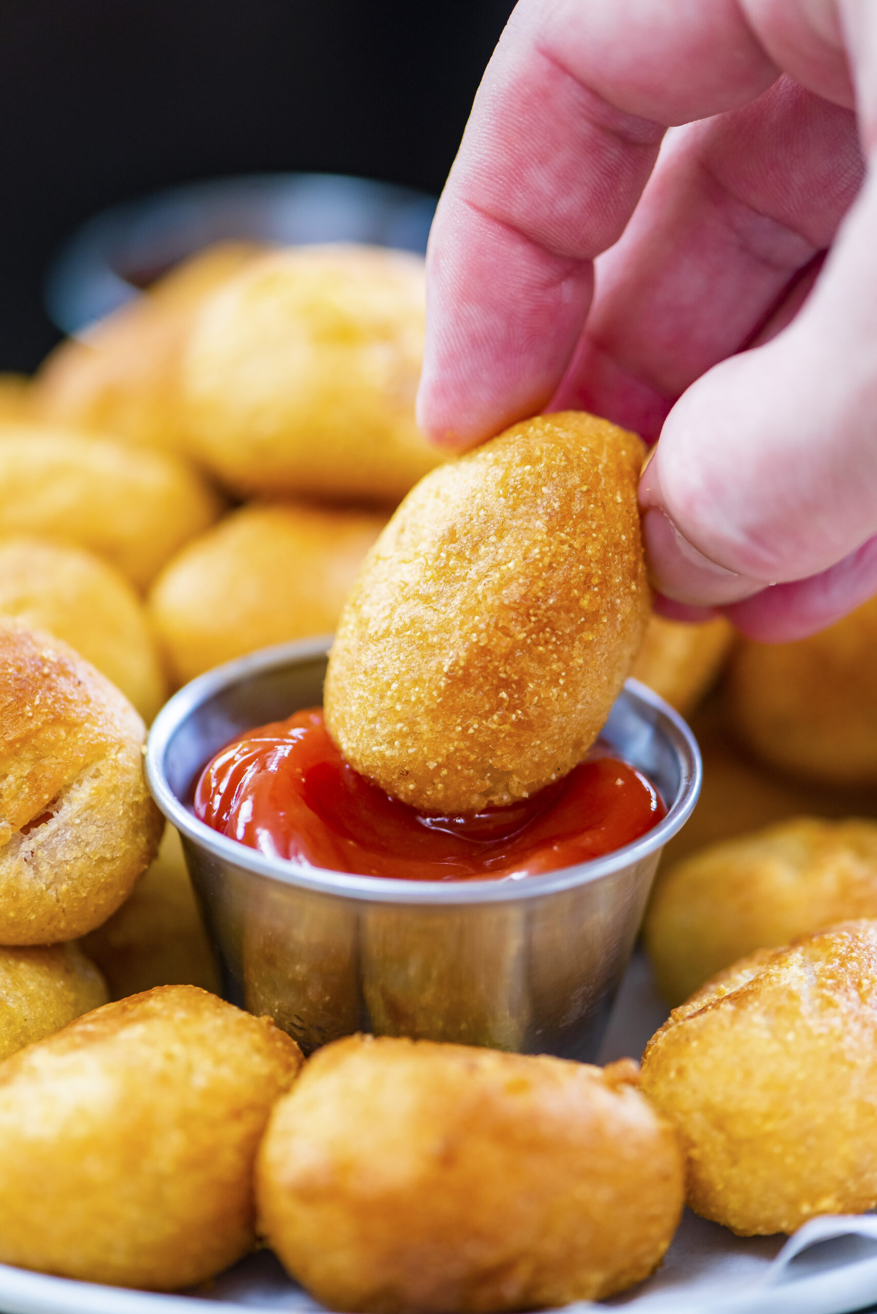 Hand dipping a mini corn dog in ketchup.