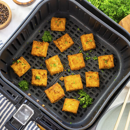 Cooked tofu in an air fryer basket.