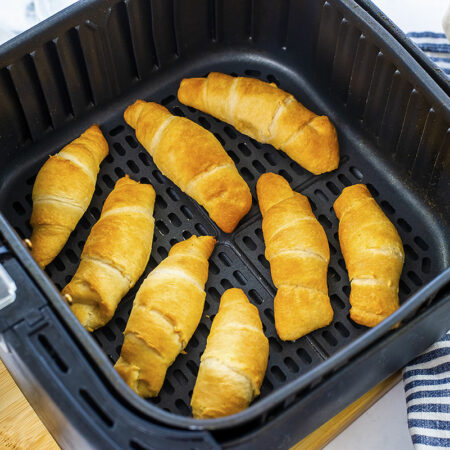 Eight crescent rolls in an air fryer basket.