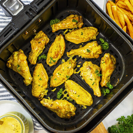 Air fryer basket with several chicken wings in it.