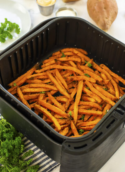 Air fryer basket full of sweet potato fries in front of a sweet potato.,