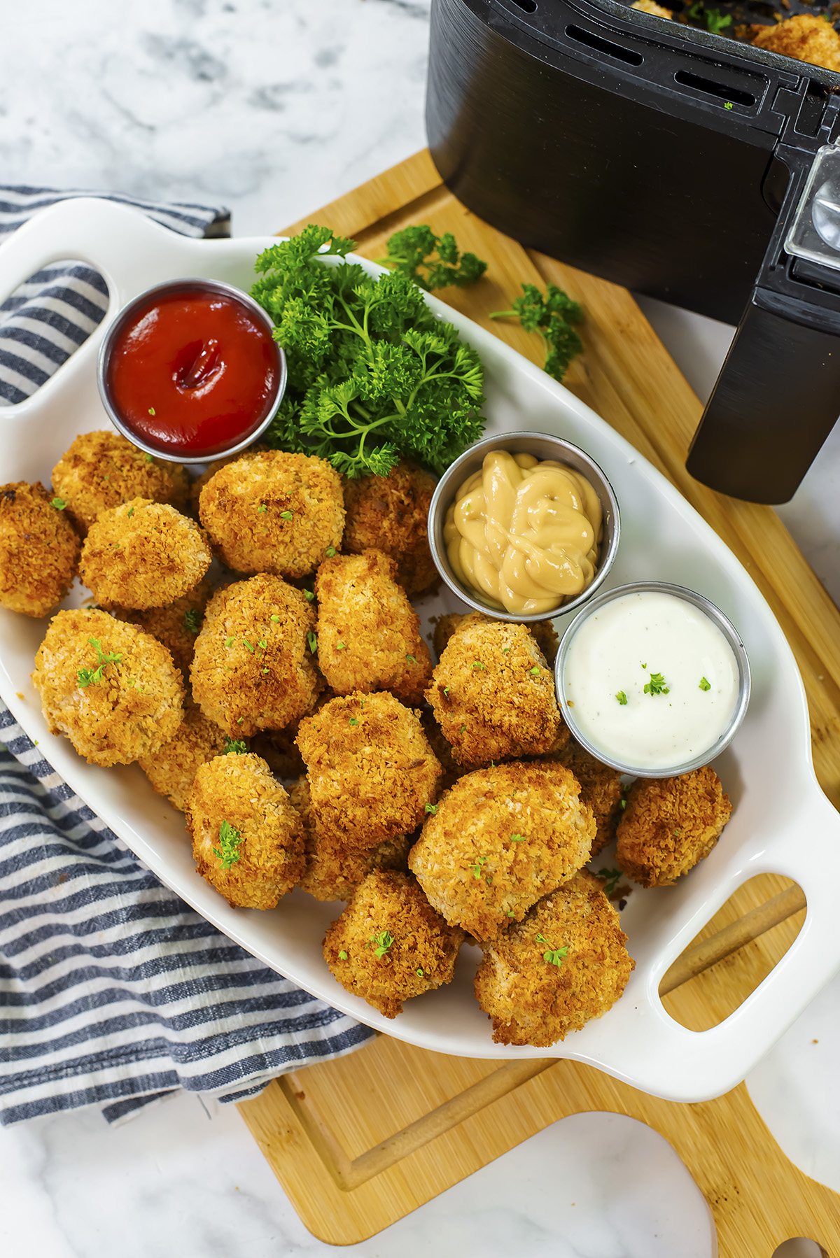 A serving tray with tofu nuggets and dips on it in front of an air fryer.