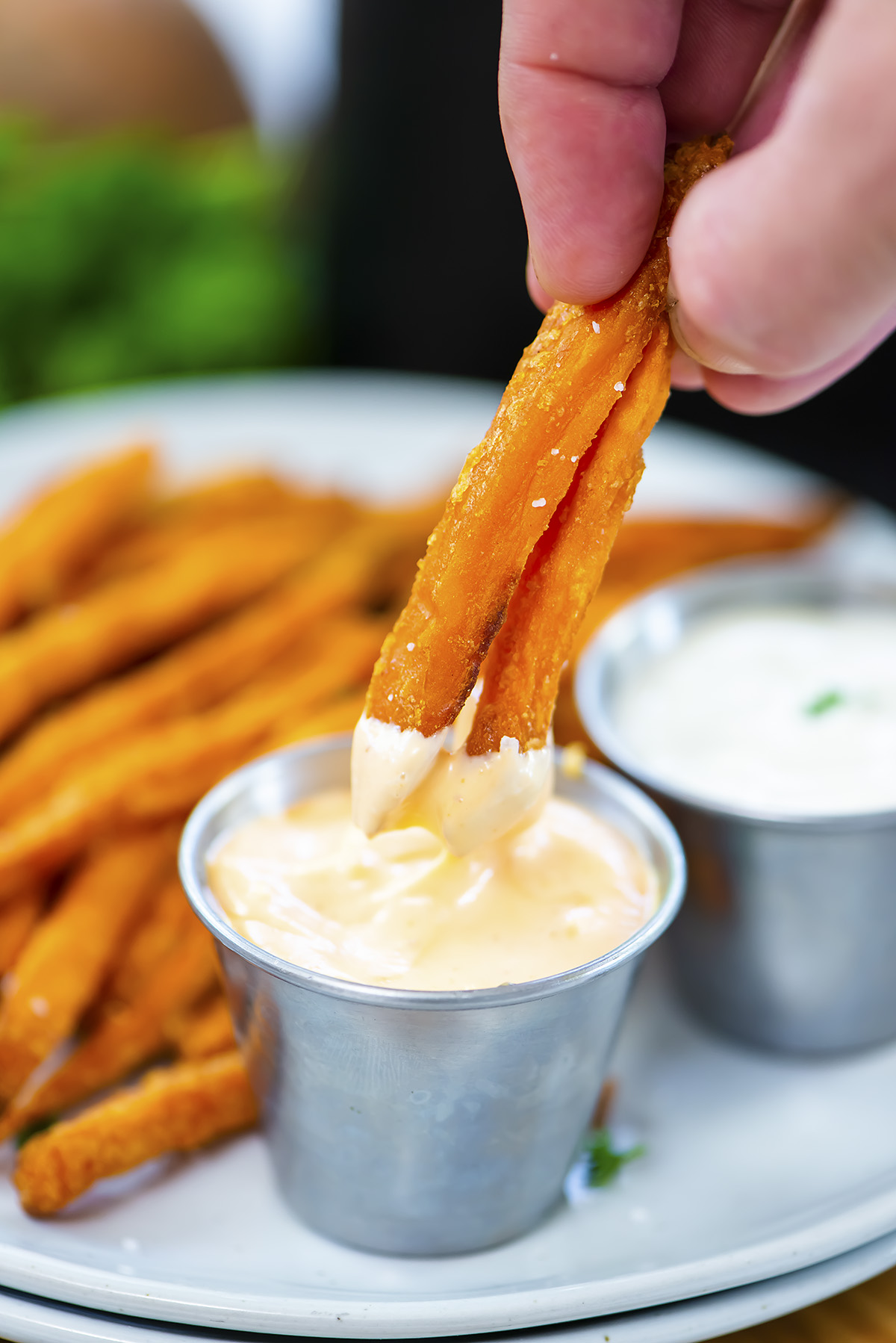 Close up of a person dipping sweet potato fries into spicy mayo dip.
