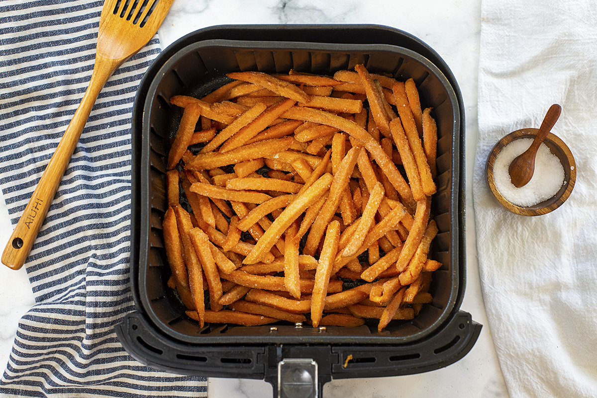 Overhead view of raw sweet potato fries in an air fryer basket.