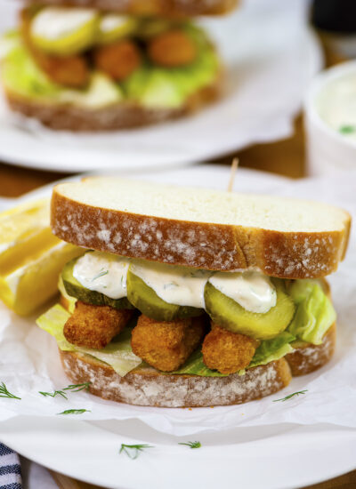 Close up of a fish stick sandwich topped with pickles and tartar sauce.