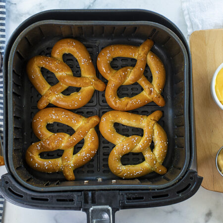 Four large pretzels in an air fryer basket.