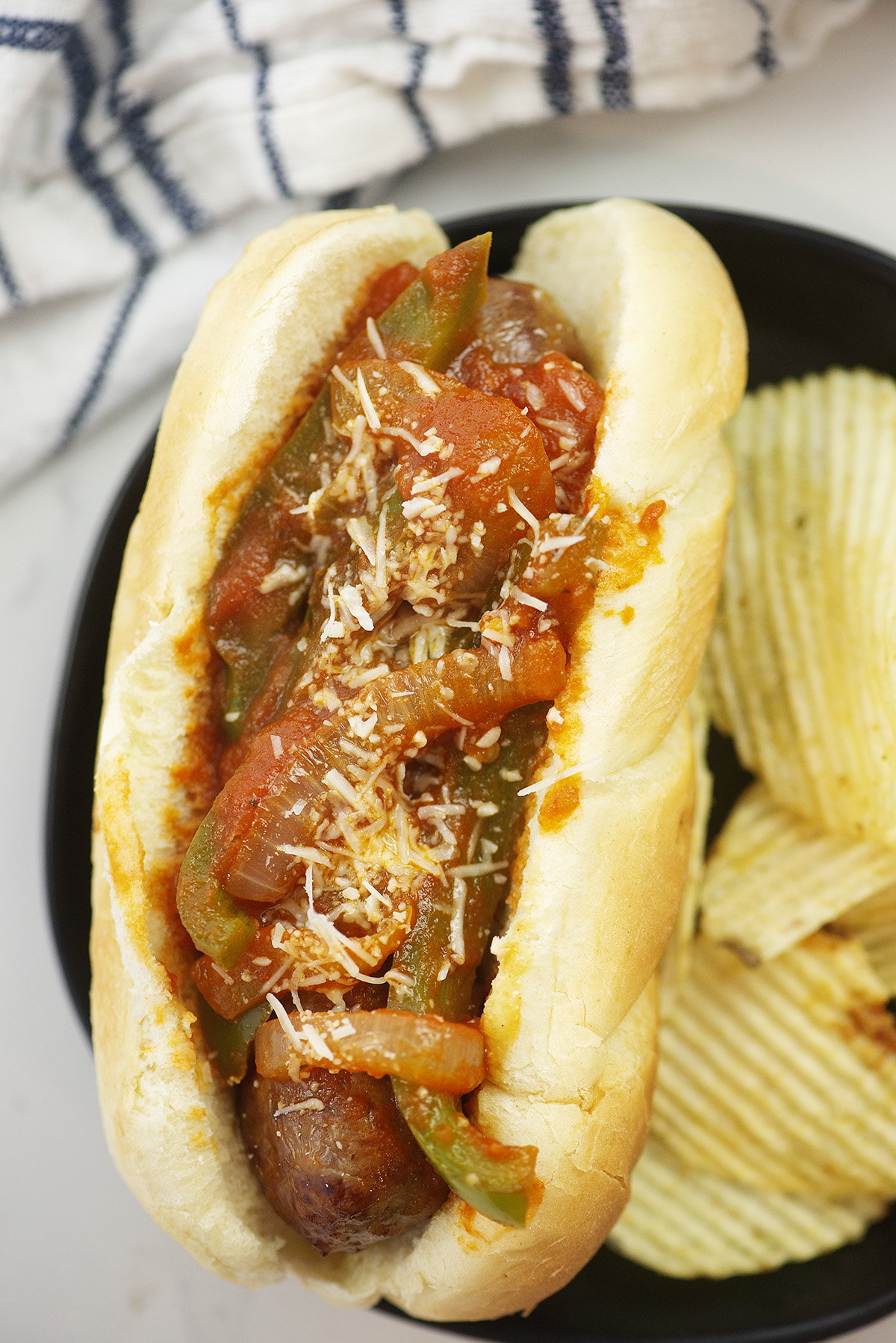 Close up of an Italian sausage on a bun topped with marinara and onions.